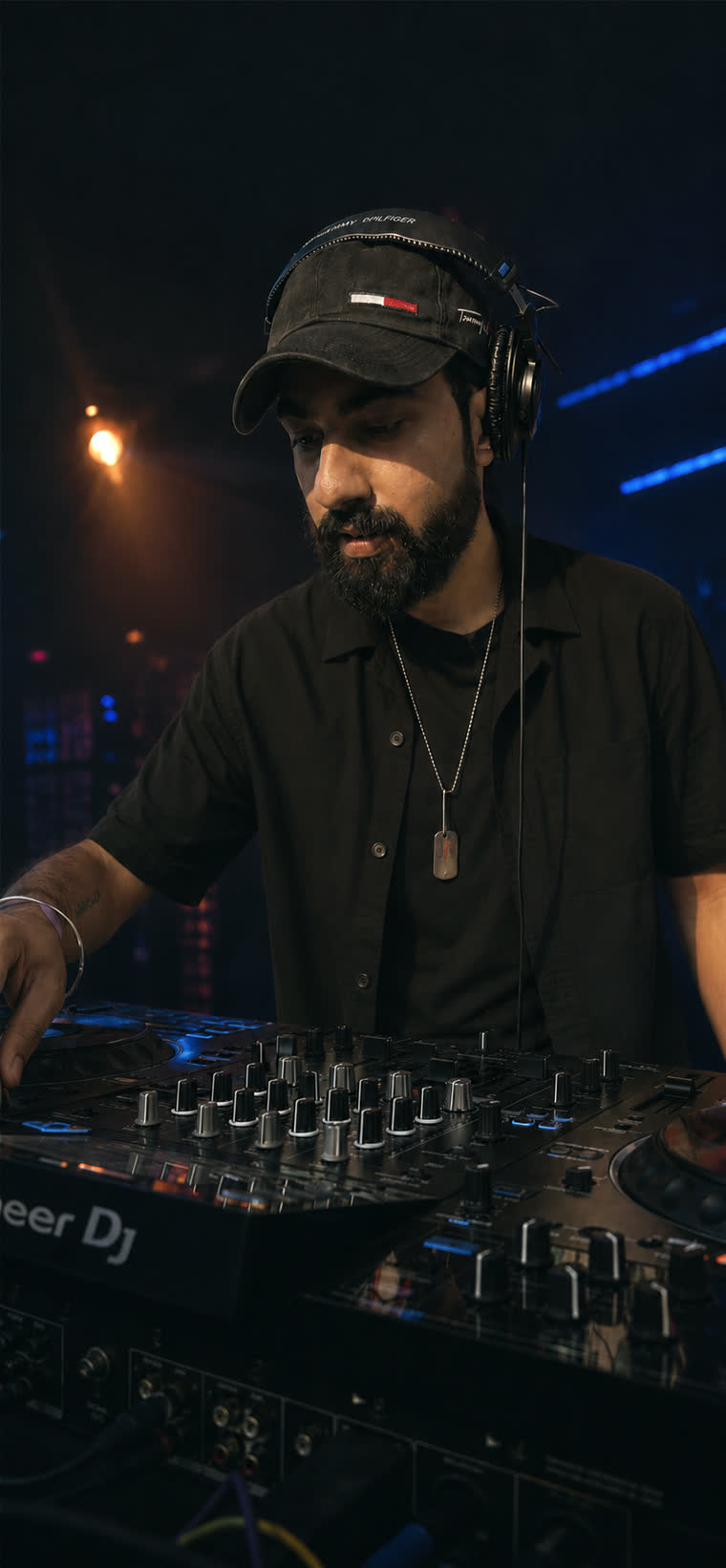DJ Hotdrop at a Pioneer mixer in a dark club, cap and headphones on